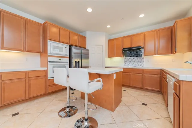 a kitchen with stainless steel appliances kitchen island granite countertop a refrigerator a stove a sink with island chairs and cabinets