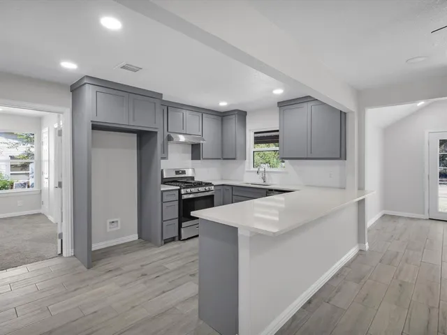 a kitchen with stainless steel appliances granite countertop a refrigerator a sink dishwasher a stove and white countertops with wooden floor