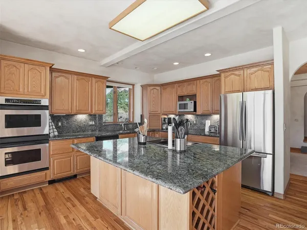 a kitchen with stainless steel appliances granite countertop a refrigerator a stove and a sink with wooden floors