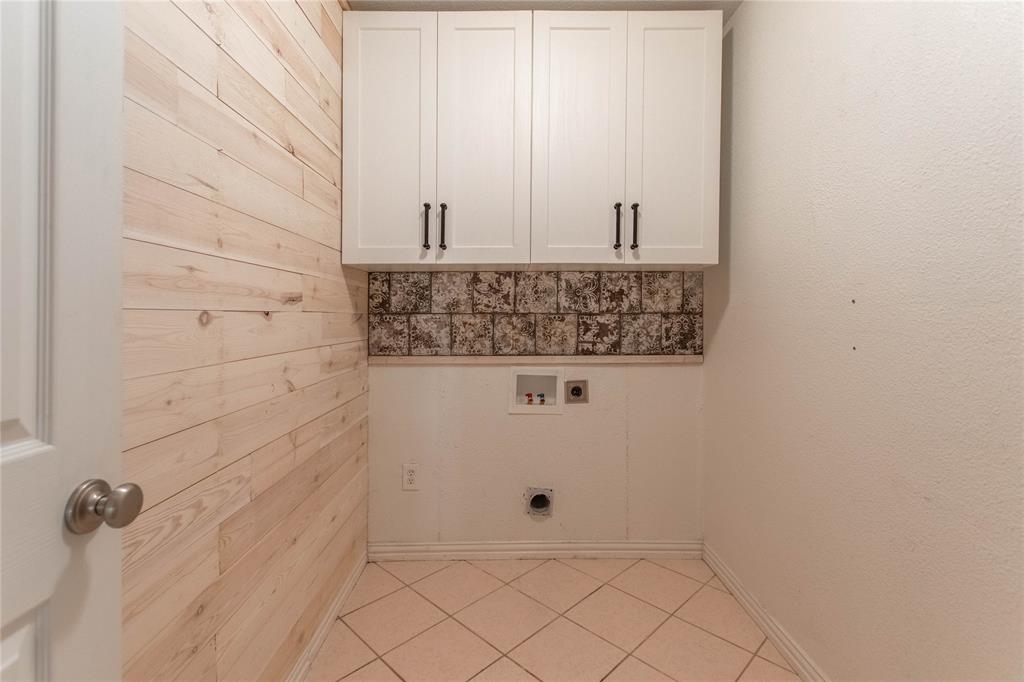 308 Sanders Road Denton, TX 76210 - Photo 19 of 31 Light wood-paneled accent wall with upper white cabinetry and dark hardware