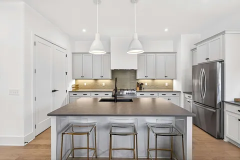 a kitchen with granite countertop a refrigerator a stove a sink and chairs