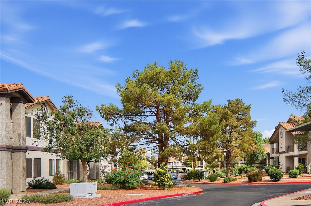 1575 West Warm Springs Road, Unit 2212 Henderson, NV 89014 - Photo 27 of 29 Mature trees and neat landscaping frame the neighborhood drive under a clear blue sky.