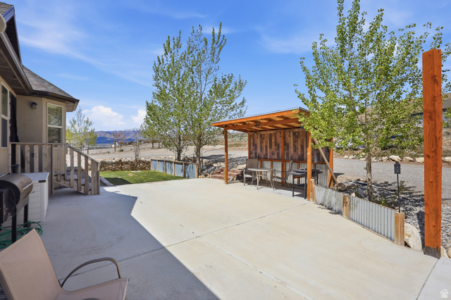 1588 West Rim Rock Drive Stockton, UT 84071 - Photo 45 of 61 Spacious concrete patio featuring a covered seating area with wood paneling, a small grassy section, and mature trees