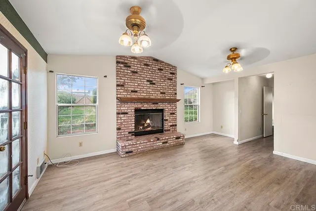 an empty room with wooden floor fireplace and windows