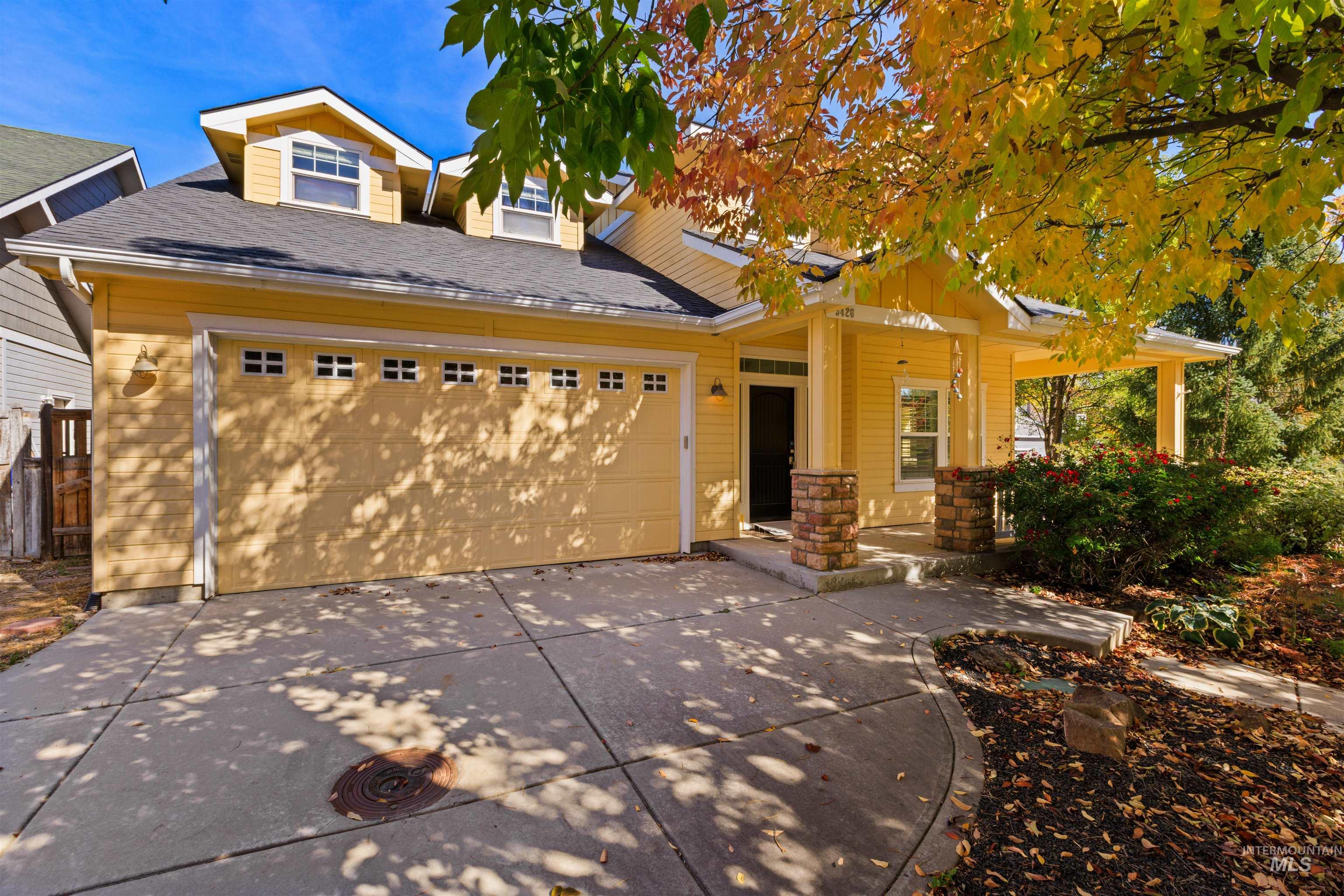 Yellow exterior with a covered porch, stone-clad columns, an attached garage, and dormer windows