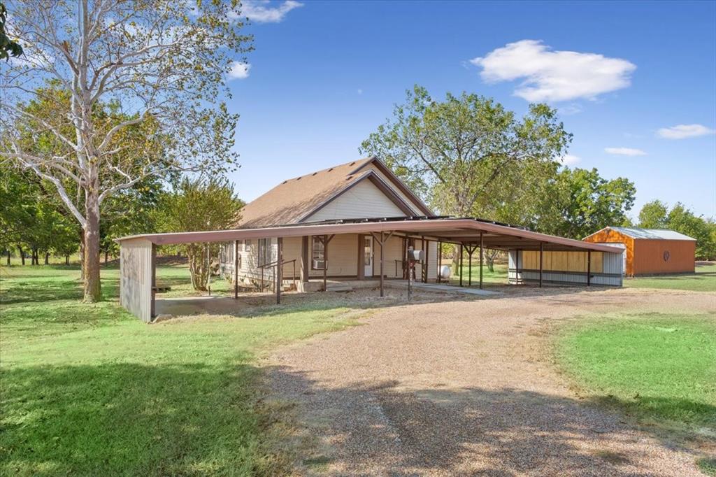 4246 Old Caufield Ranch Road McGregor, TX 76657 - Photo 31 of 31 Gable roof structure with a covered porch entry, expansive gravel driveway, long attached carport, and a detached outbuilding