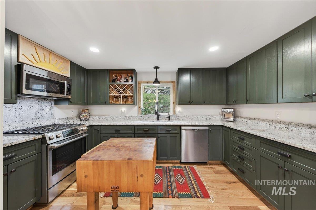 239 Tollgate Road Boise, ID 83716 - Photo 5 of 50 Kitchen featuring green cabinetry, stainless steel appliances, light wood-type flooring, hanging light fixtures, and light stone counters