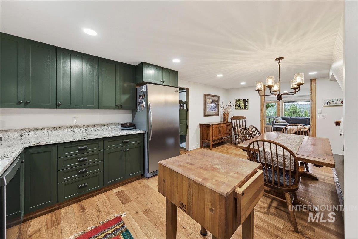 239 Tollgate Road Boise, ID 83716 - Photo 7 of 50 Kitchen featuring green cabinetry, a chandelier, freestanding refrigerator, light wood-style flooring, and light stone countertops