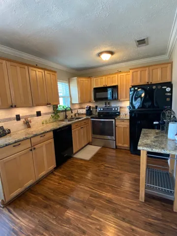 a kitchen with stainless steel appliances granite countertop a stove a sink dishwasher a refrigerator and a microwave oven on the wooden floor