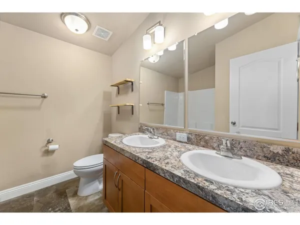 a bathroom with a granite countertop double vanity sink a mirror and a toilet