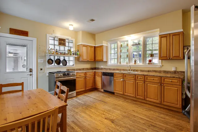 a kitchen with stainless steel appliances kitchen island granite countertop a stove a sink dishwasher and white cabinets with wooden floor