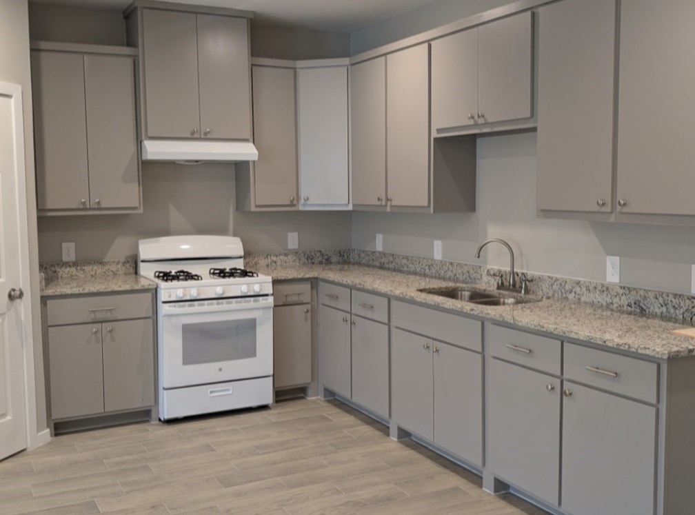 7745 Swiftwater Lane, Unit A Houston, TX 77075 - Photo 11 of 33 This modern kitchen features abundant storage with sleek, light grey cabinetry and granite-look countertops wrapping around the corner. It is equipped with a white gas range and hood, a double basin stainless steel sink, and consistent wood-look tile flooring.