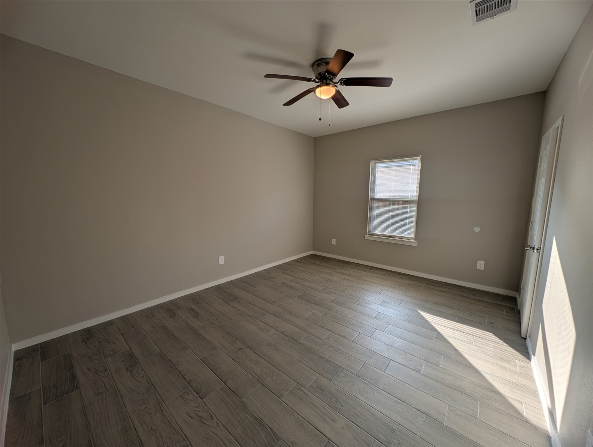 7745 Swiftwater Lane, Unit A Houston, TX 77075 - Photo 14 of 33 Bedroom is painted in a neutral tan color and features attractive grey wood-look tile flooring throughout. Natural light enters through a single window with blinds, and a ceiling fan with a light fixture provides both air circulation and illumination.
