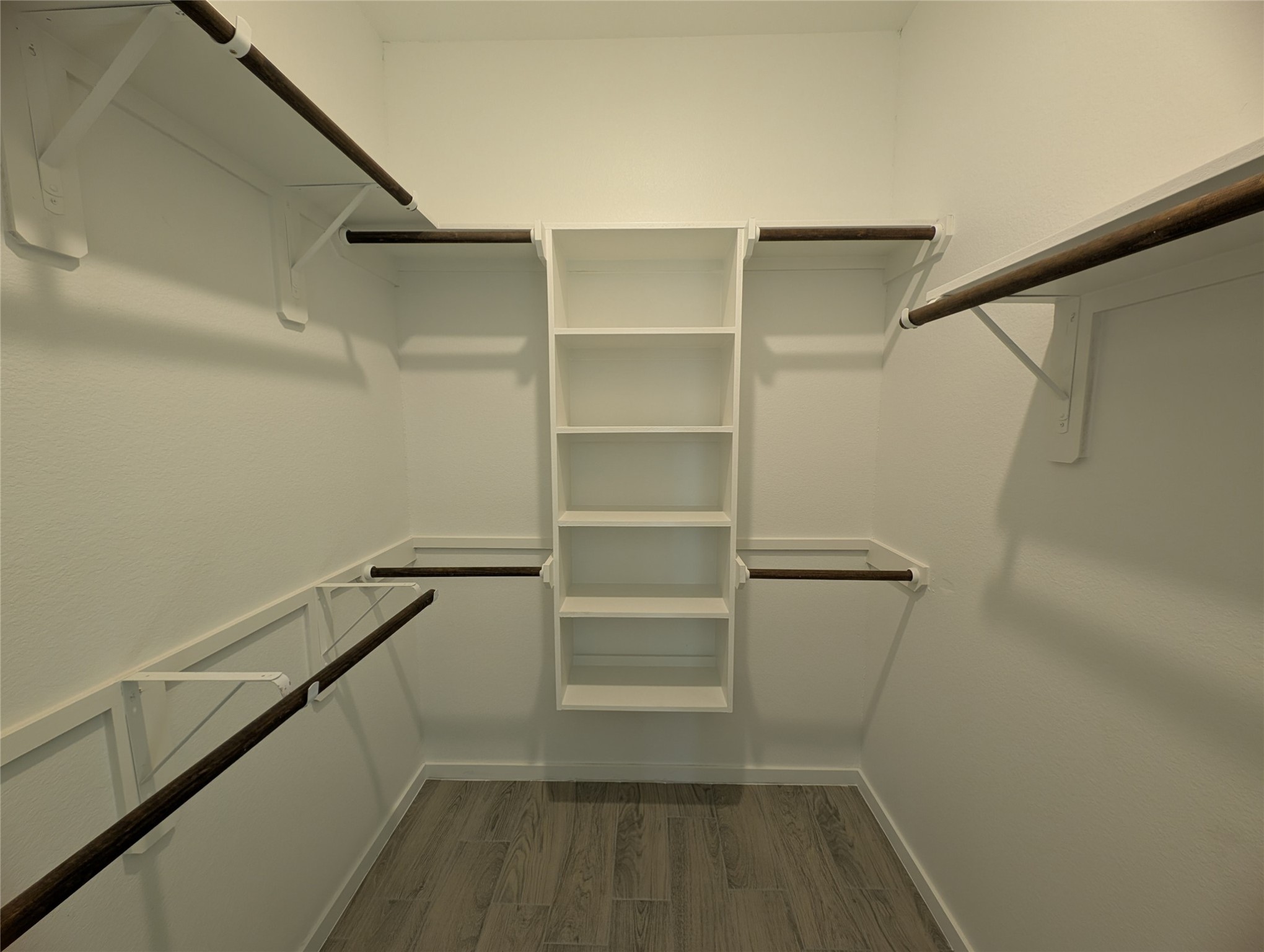 7745 Swiftwater Lane, Unit A Houston, TX 77075 - Photo 16 of 33 This well-organized closet features a convenient built-in shelving unit centered between multiple dark-rod hanging areas and upper white shelving along three walls. The light white walls and grey wood-look tile flooring contribute to a clean, modern storage space.