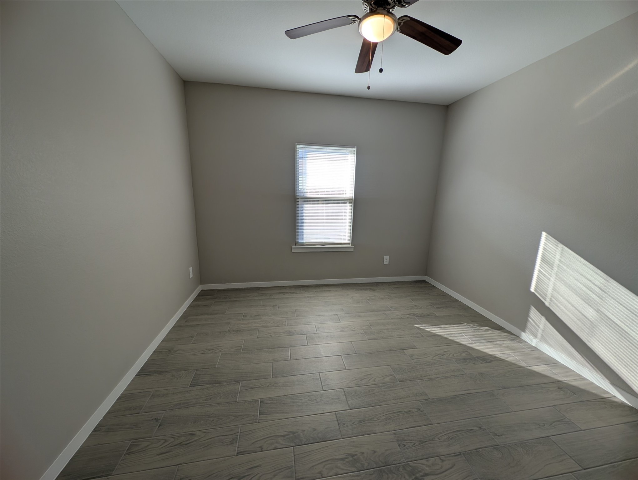7745 Swiftwater Lane, Unit A Houston, TX 77075 - Photo 22 of 33 The other Bedroom is a spacious and neutral space, featuring sleek grey wood-look tile flooring and light grey/tan walls, complemented by bright natural light filtering through the blinds, and a dark ceiling fan for comfort.