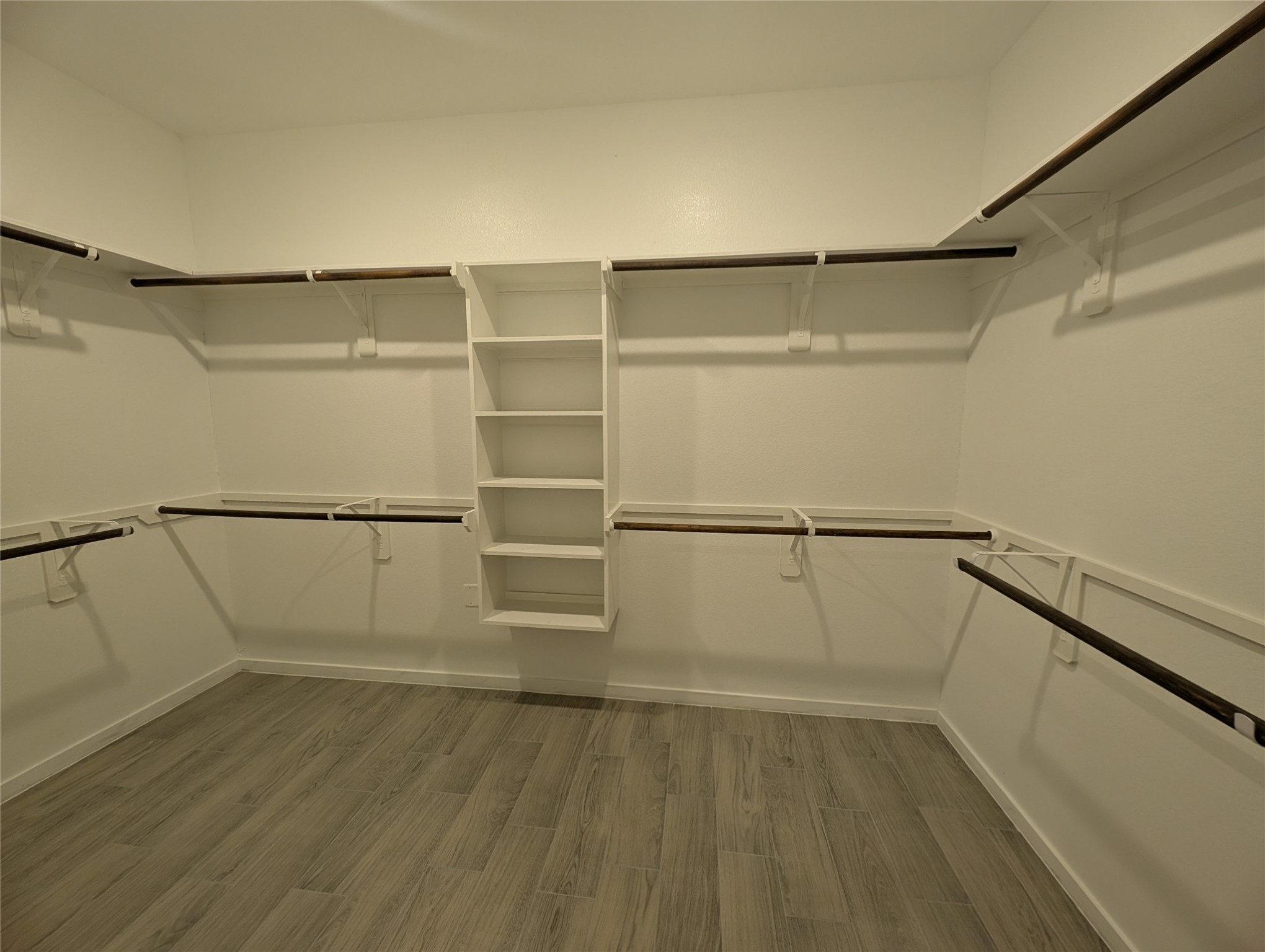 7745 Swiftwater Lane, Unit A Houston, TX 77075 - Photo 28 of 33 This spacious walk-in closet is designed for maximum storage, featuring wraparound shelving and multiple hanging rods with dark wood accents for both him and her. A central built-in organizer provides additional shelf space for folded items.