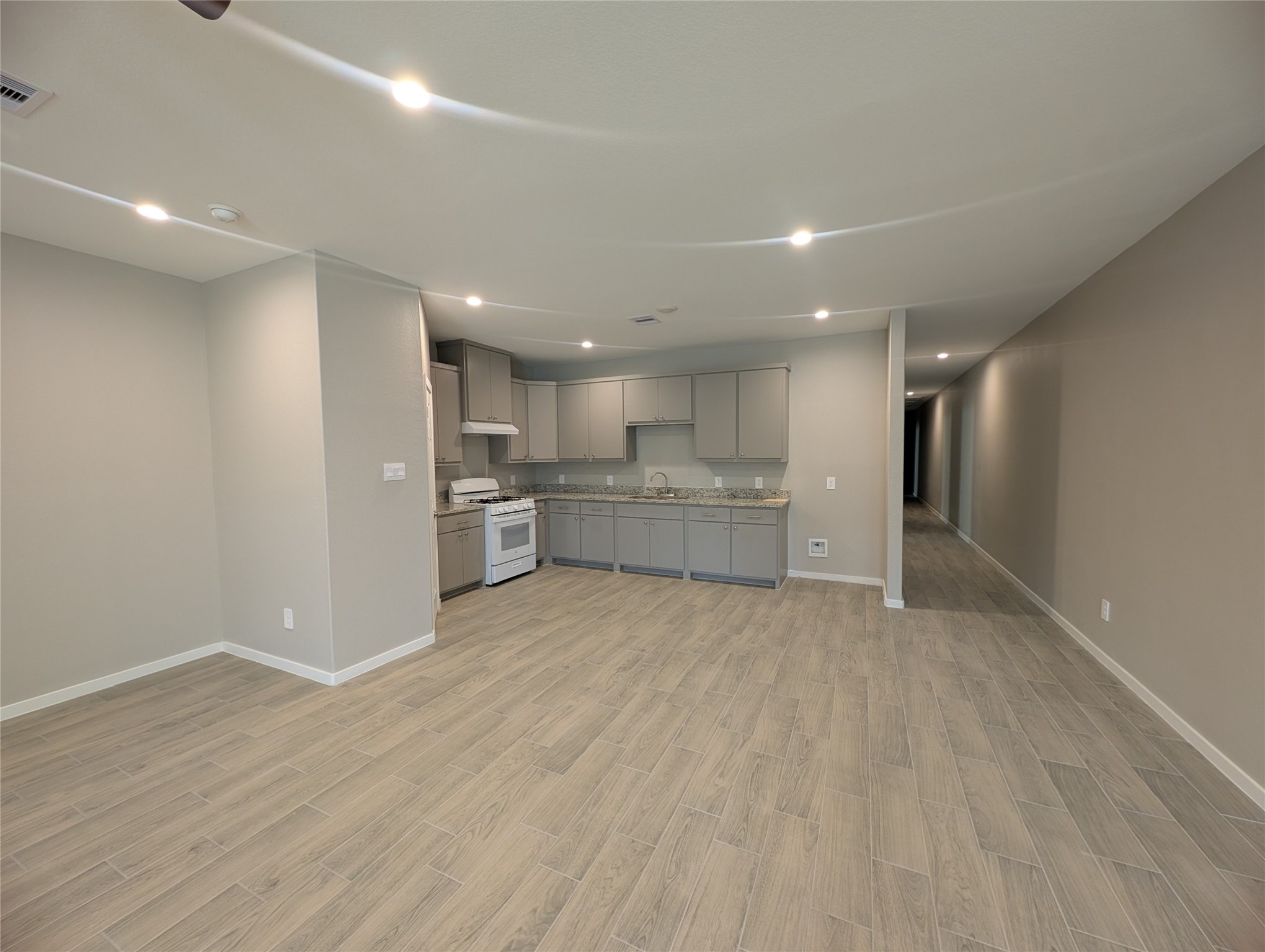 7745 Swiftwater Lane, Unit A Houston, TX 77075 - Photo 7 of 33 This spacious open-concept living area seamlessly integrates the living room and kitchen, featuring connected light grey wood-look tile flooring throughout. The kitchen boasts modern grey cabinetry and a white stove, illuminated by bright recessed ceiling lights across the entire space.