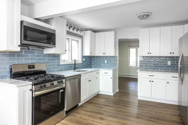 a kitchen with granite countertop a stove top oven a sink dishwasher and white cabinets with wooden floor