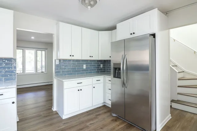 a kitchen with stainless steel appliances granite countertop a refrigerator a sink and white cabinets with wooden floor
