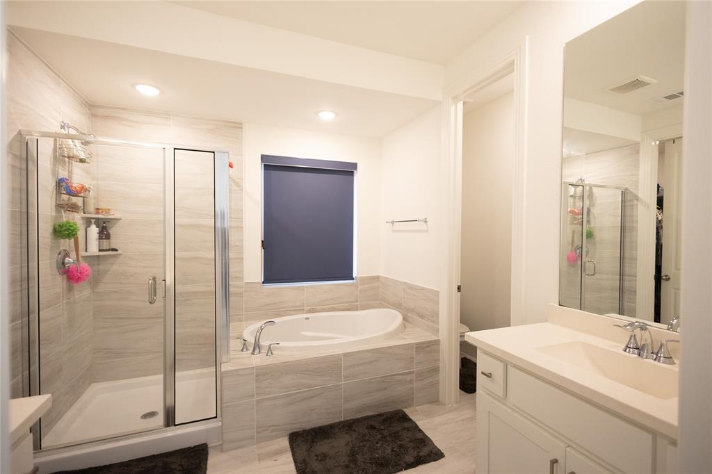 3017 Andorra Road McKinney, TX 75071 - Photo 20 of 40 Walk-in shower with clear glass enclosure, a built-in soaking tub, a single vanity with an integrated sink, and a rectangular wall-mounted mirror