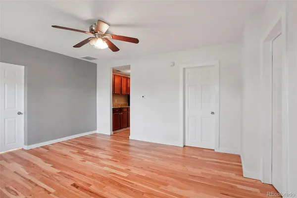 a view of an empty room with wooden floor and a ceiling fan