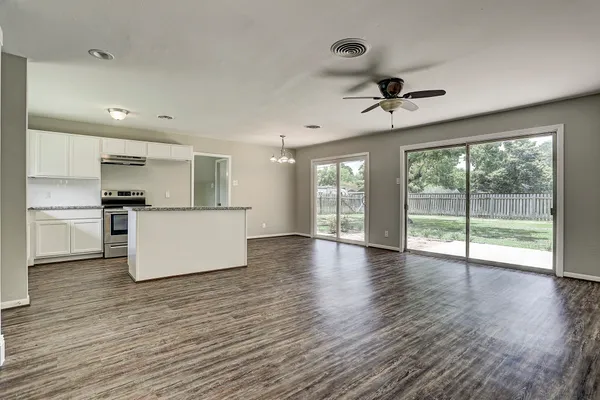 a view of an empty room with wooden floor and a kitchen