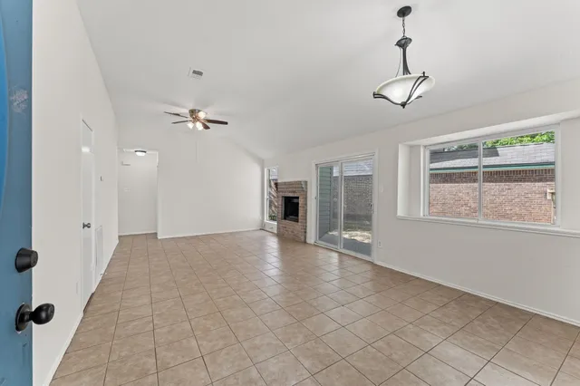 a view of an empty room with chandelier fan and windows