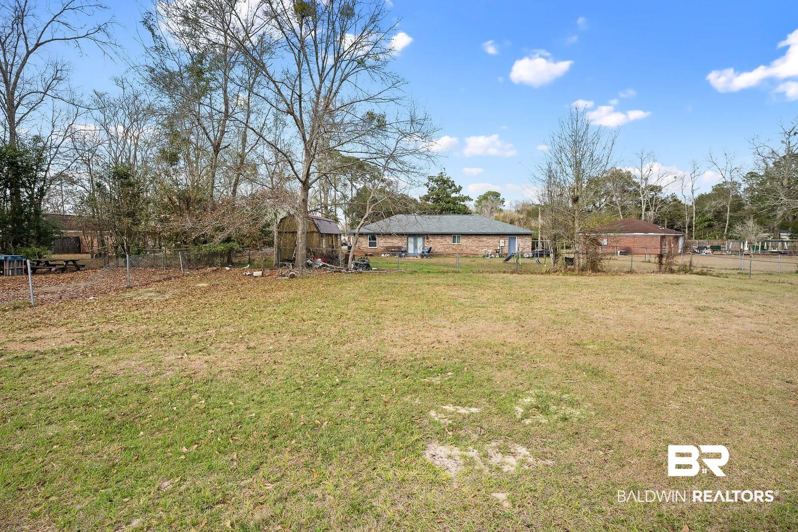 635 East Azalea Avenue Foley, AL 36535 - Photo 17 of 18 Expansive grass lawn featuring a wood storage shed and a chain-link fence