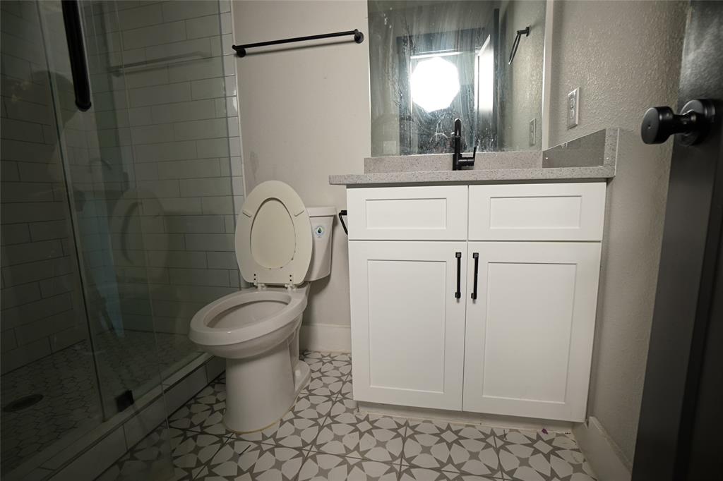 1764 Palladio Loop Princeton, TX 75407 - Photo 35 of 40 Bathroom featuring a glass-enclosed shower with subway tile, a white toilet, a vanity with a light-toned countertop, white cabinetry with black pulls, and patterned floor tiling