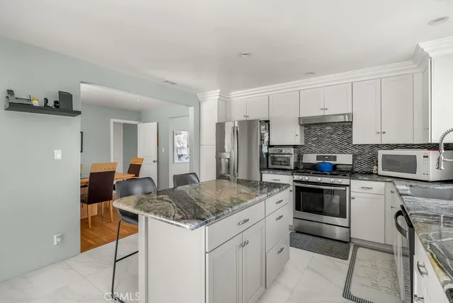 a kitchen with stainless steel appliances granite countertop a stove top oven a sink a refrigerator and white cabinets