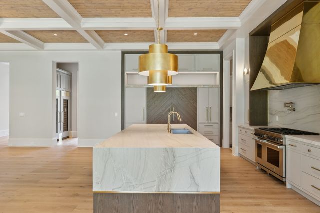 a hall with kitchen island granite countertop a sink stainless steel appliances wooden floor and a large window