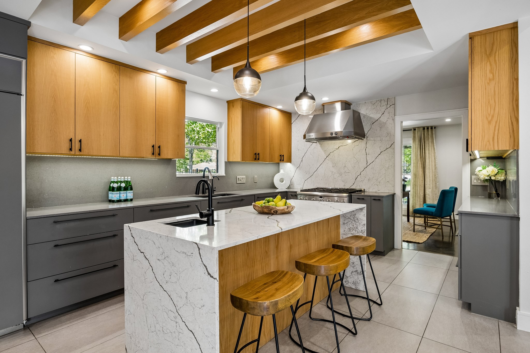 Reimagined chef's kitchen for modern living, this stunning space pairs large format tile with raised ceilings, warm wood beams, and designer M&M Lighting for a look that feels both timeless and elevated.