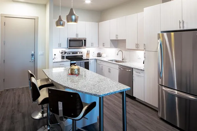 a kitchen with stainless steel appliances granite countertop a dining table chairs refrigerator and microwave