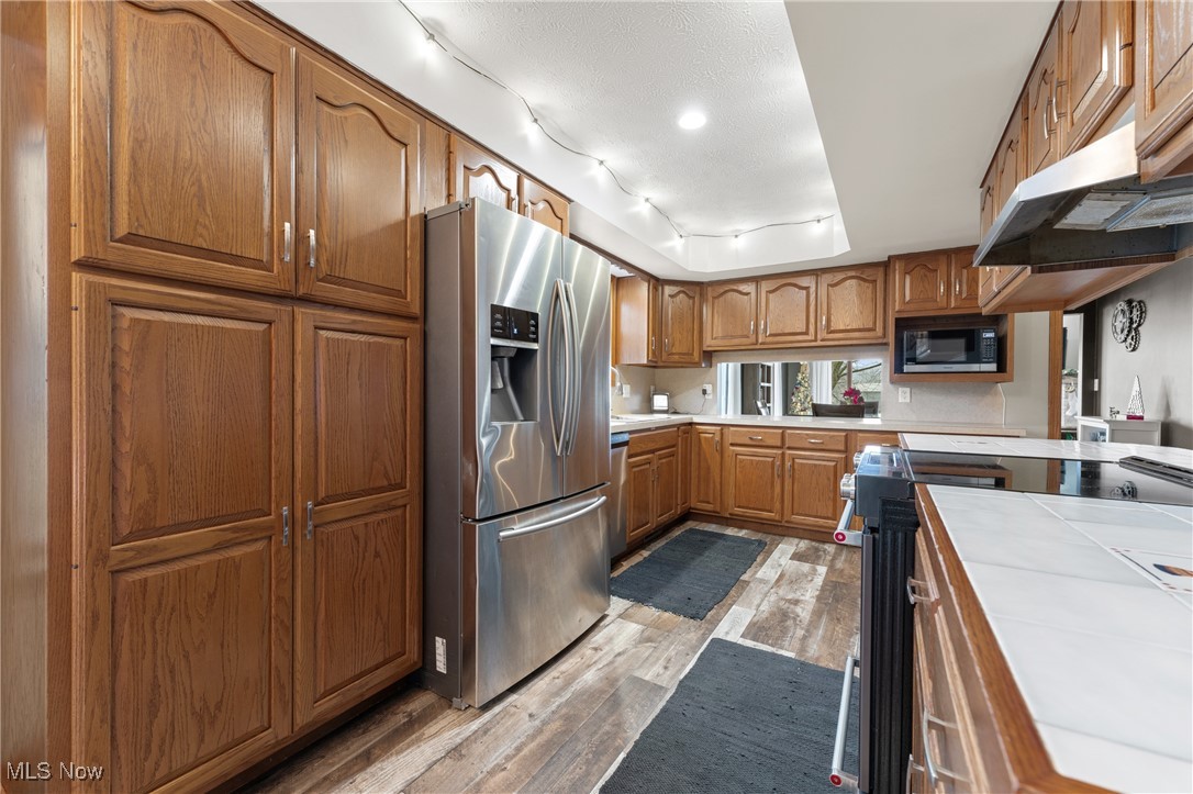 645 Killinger Road Clinton, OH 44216 - Photo 8 of 50 Kitchen with built in microwave, tile counters, stainless steel refrigerator with ice dispenser, range with electric stovetop, and light hardwood / wood-style floors