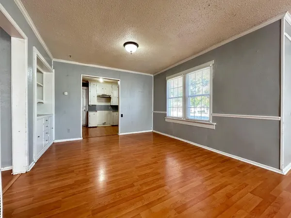 a view of empty room with wooden floor and kitchen view
