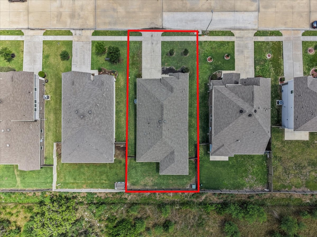 2320 Rosemary Street Rosenberg, TX 77469 - Photo 40 of 40 This aerial photo shows a house outlined in red, situated in a suburban neighborhood. It features a driveway leading to a two-car garage, a neatly maintained lawn, and is flanked by similar houses on either side. The backyard is bordered by a fence and backs onto a green space.