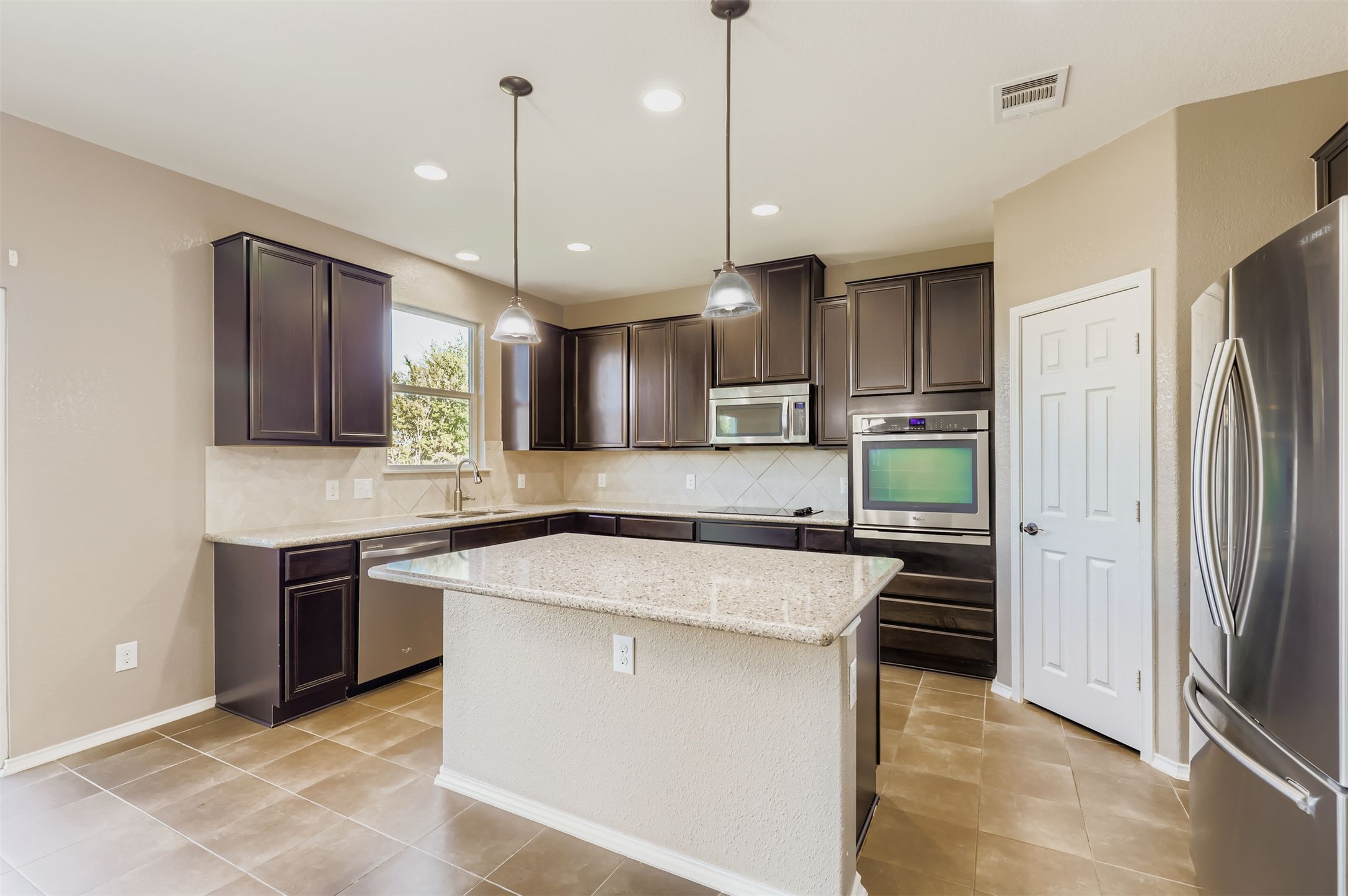 18808 Star Gazer Way Pflugerville, TX 78660 - Photo 10 of 27 Kitchen featuring dark brown cabinets, stainless steel appliances, pendant lighting, a kitchen island, and backsplash