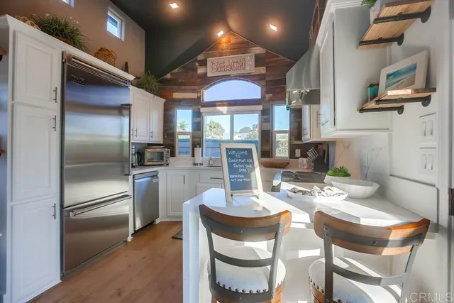 a kitchen with stainless steel appliances granite countertop a refrigerator a sink dishwasher a dining table and chairs with wooden floor