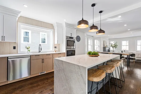 a kitchen with stainless steel appliances granite countertop a stove a sink a refrigerator a dining table and chairs with wooden floor