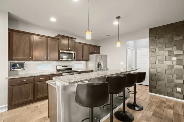 a kitchen with stainless steel appliances granite countertop a sink a stove a refrigerator cabinets and chairs