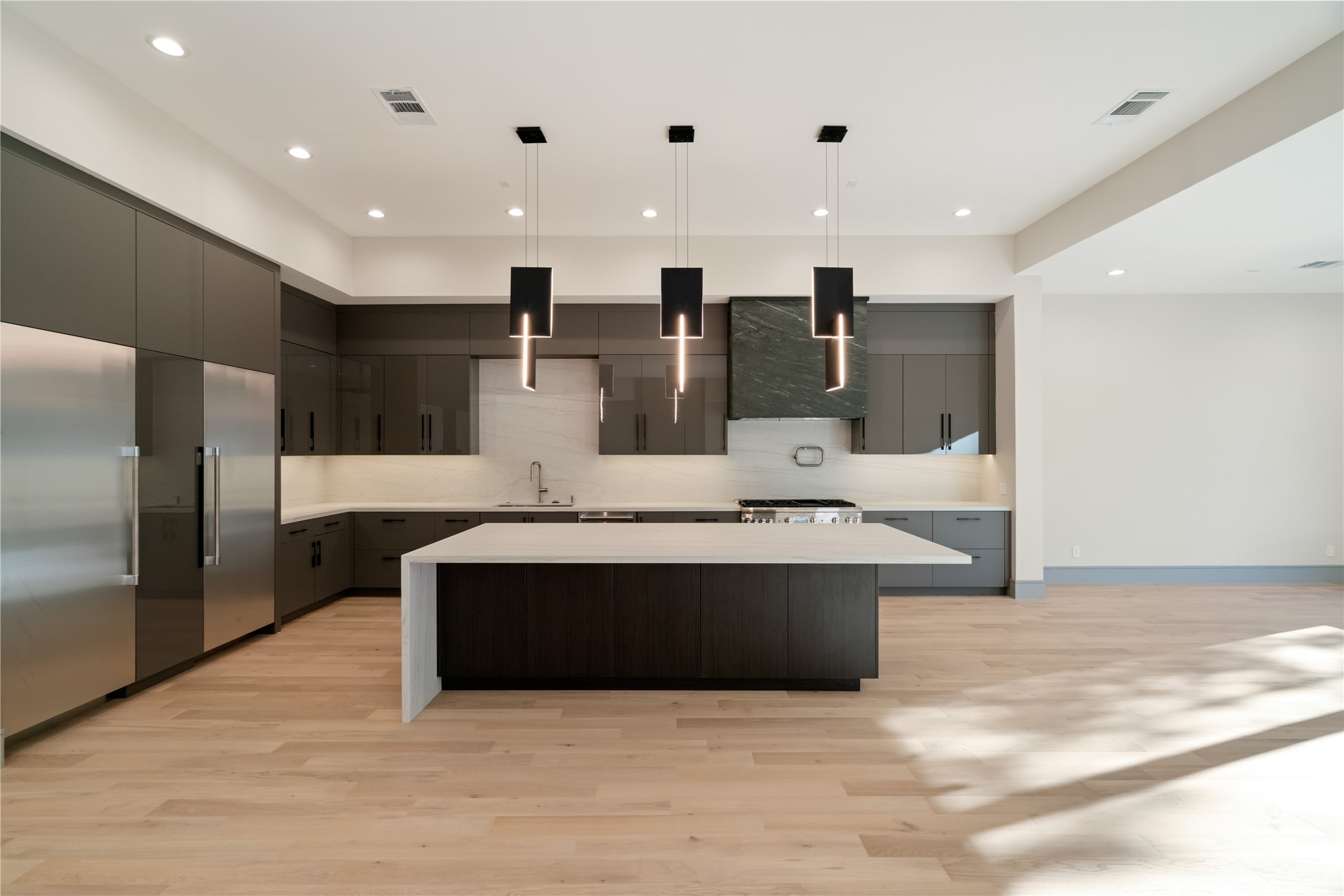 47 Pronghorn Place Spring, TX 77389 - Photo 9 of 44 This photo showcases a modern kitchen with sleek cabinetry, a large central island, and contemporary pendant lighting. It features stainless steel appliances and light wood flooring, creating a spacious and elegant atmosphere.