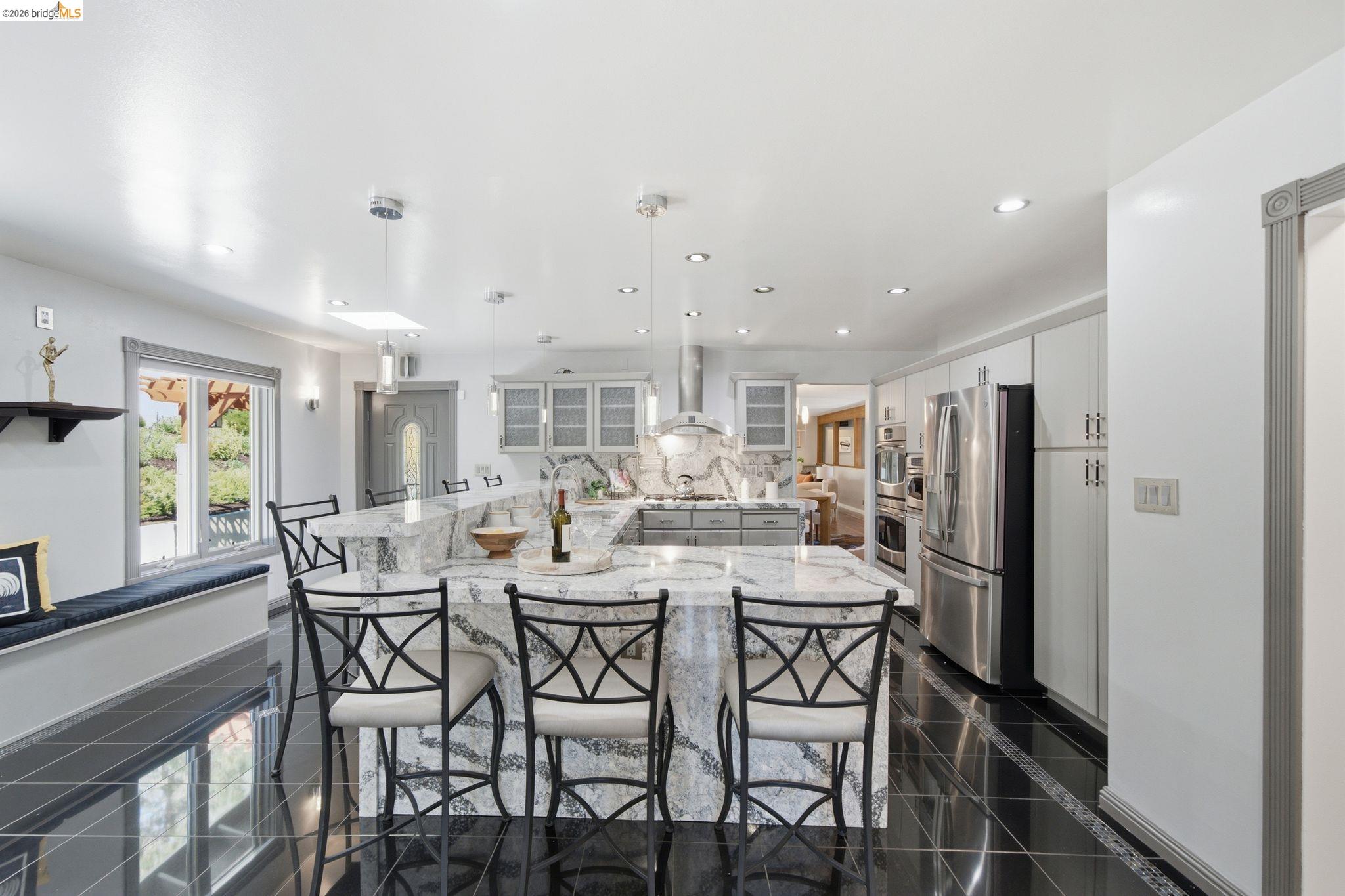11133 Golf Links Road Oakland, CA 94605 - Photo 16 of 57 Kitchen featuring a large central island with waterfall-edge countertop, black tile flooring, light gray cabinetry, and stainless steel appliances