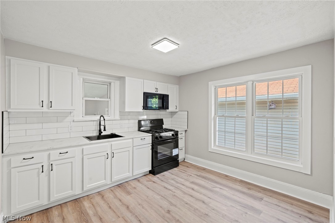 1218 Briggle Road Akron, OH 44320 - Photo 12 of 40 Kitchen featuring wood-finish flooring, white cabinetry with matte black hardware, white subway tile backsplash, white countertops, and a black gas range
