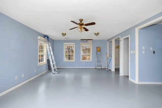 an empty room with chandelier fan and windows