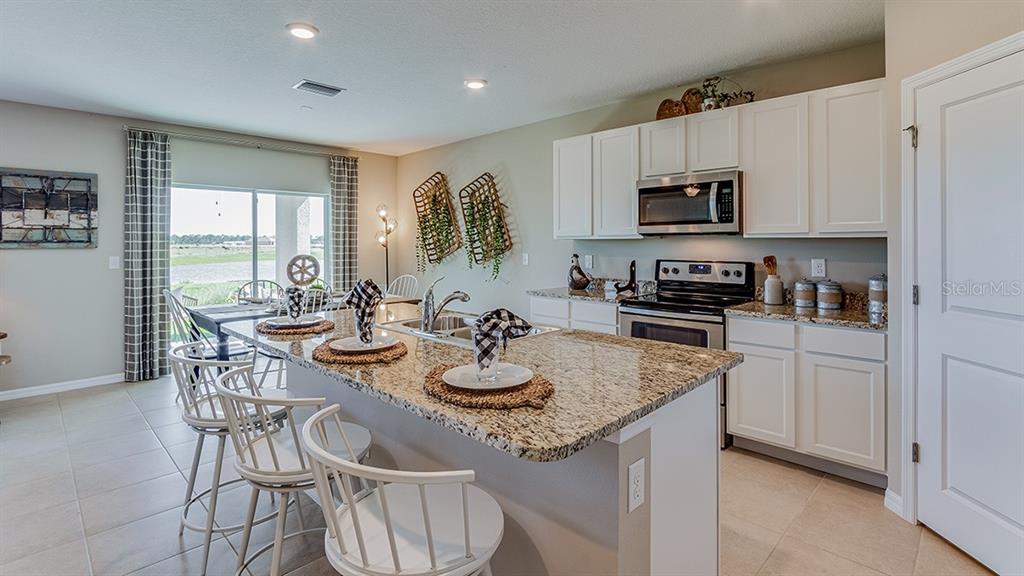 18106 Wheathouse Place Lakewood Ranch, FL 34211 - Photo 3 of 43 a kitchen with stainless steel appliances granite countertop a sink a stove a table and chairs