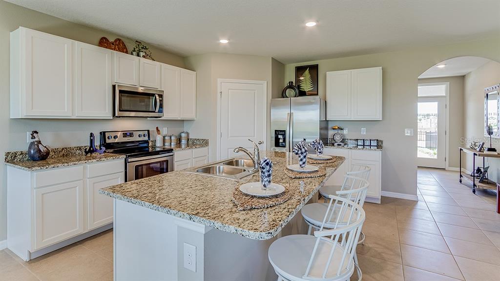 18106 Wheathouse Place Lakewood Ranch, FL 34211 - Photo 4 of 43 a kitchen with stainless steel appliances kitchen island granite countertop a sink a stove a table and chairs