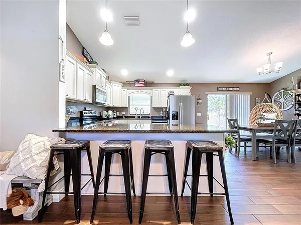 a kitchen with granite countertop a refrigerator a stove a sink and a dining table with wooden floor