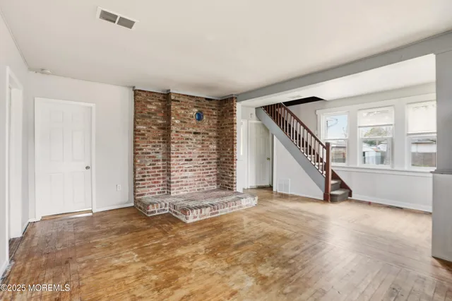 a view of an empty room with wooden floor and stairs
