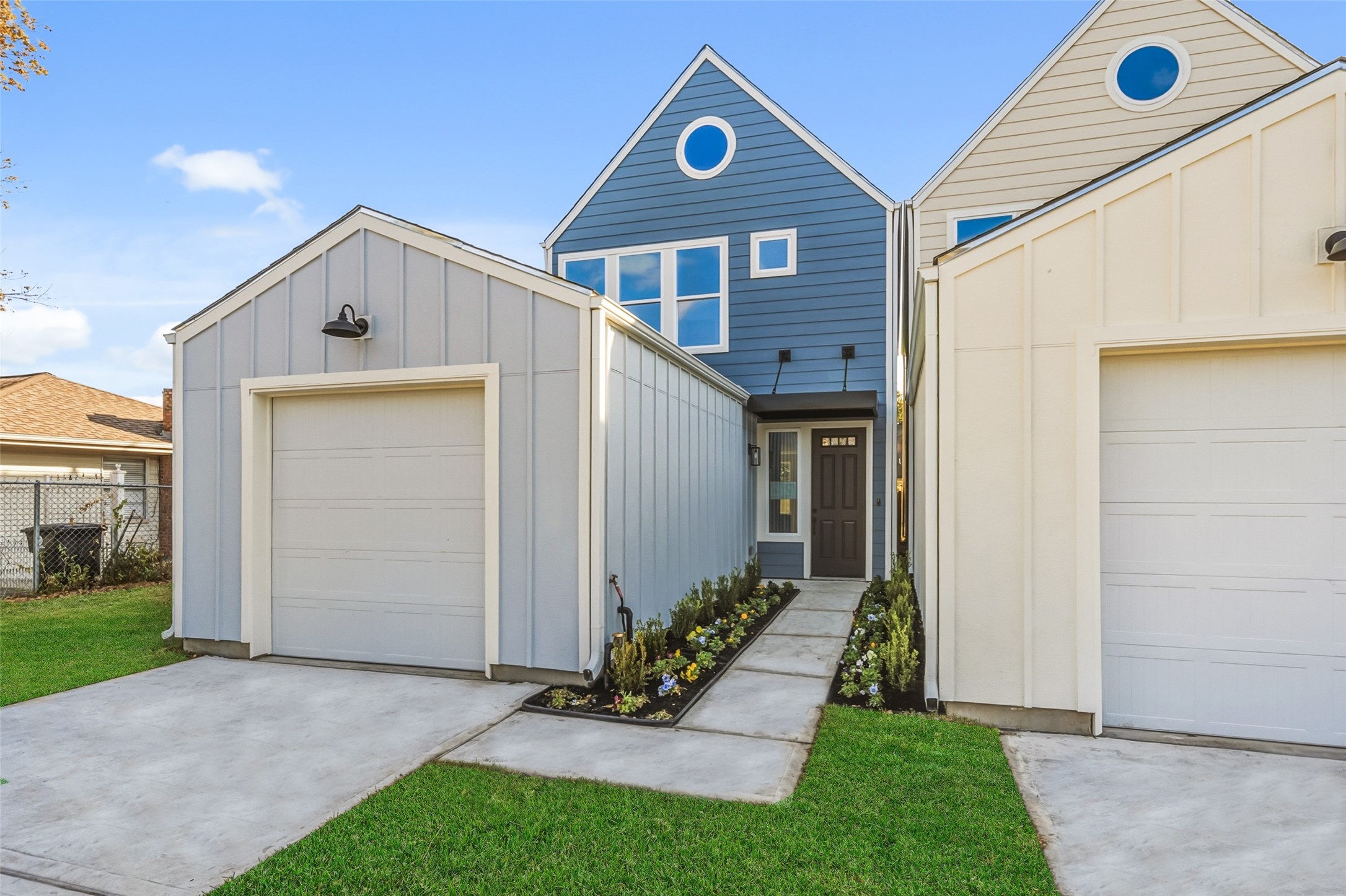 Modern two-story home with a fresh exterior featuring blue and white siding. It includes a single-car garage, a neat driveway, and a charming walkway with landscaped borders leading to the front door.