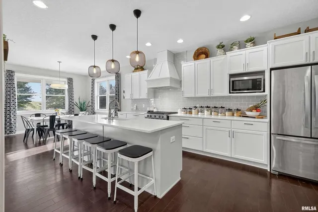 a kitchen with stainless steel appliances granite countertop a stove a sink a refrigerator and a dining table with wooden floor